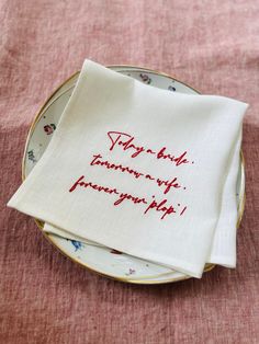 two napkins with red writing on them sitting on top of a white and gold plate