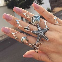 a woman's hand with five different rings on it, including one starfish and two seashells