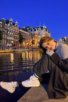 a woman sitting on the edge of a body of water with buildings in the background