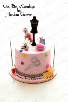 a pink cake decorated with sewing supplies on top of a white tablecloth and black mannequin