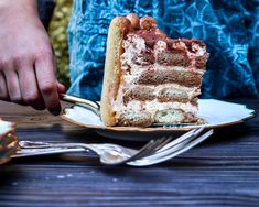 a piece of cake on a plate being held by a person's hand with silverware