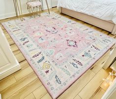 a pink and blue rug on the floor in a room with white walls, hardwood floors and a bed