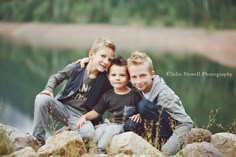 three young boys are posing for a photo by the water with their arms around each other