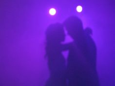 the silhouette of two people kissing in front of spotlights on a purple stage backdrop