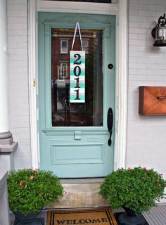 a welcome mat is on the front door of a house with two potted plants