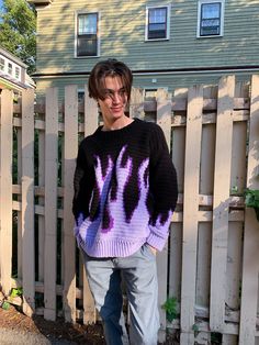 a man standing in front of a fence wearing a sweater with purple and black designs