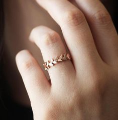 a woman's hand wearing a gold ring with leaves on the middle of it