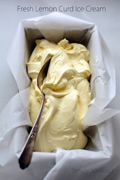 a spoon in a white container filled with yellow frosted food and paper wrappers