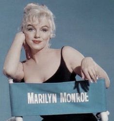 marilyn monroe sitting in a chair holding a blue sign that says marilyn monroe on it