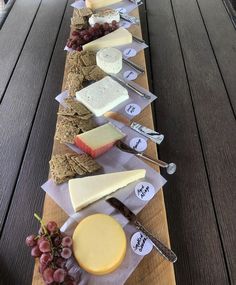 an assortment of cheeses and crackers are lined up on a long wooden table