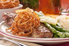 a plate with some meat and vegetables on it next to a glass of beer in the background