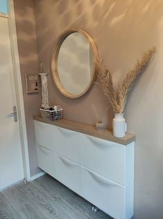 a white dresser with a round mirror above it and a plant in a vase on top