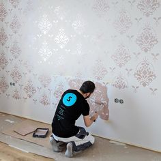 a man in black shirt painting wallpaper with blue and white stencils on it