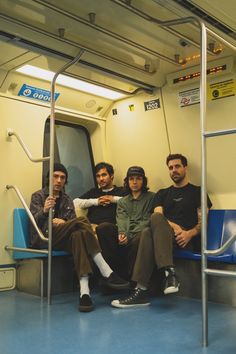 three men sitting on a subway train next to each other and looking at the camera