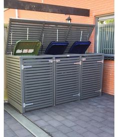 two metal trash cans sitting on top of a brick floor next to a wall with shutters