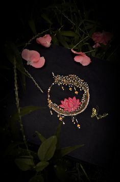 a pink flower on a black surface next to some jewelry and rose petals in the dark