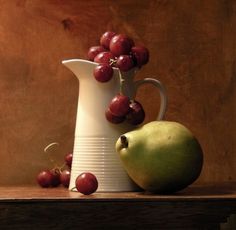 a white pitcher filled with grapes next to a green apple and some red cherries