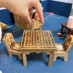 a wooden table and chairs with a hand reaching for the piece on top of it