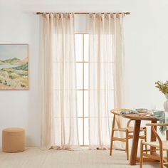 a table and chairs in front of a window with sheer curtains