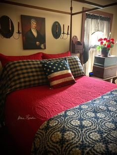 a bed with red, white and blue comforter in a bedroom next to two pictures on the wall