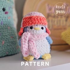 a crocheted penguin wearing a pink hat and scarf sits next to two knitted pillows