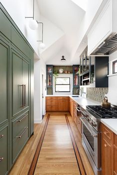 a kitchen with wood flooring and green cabinetry on the walls, along with stainless steel appliances