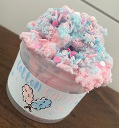 a cup filled with pink and blue sprinkles on top of a wooden table