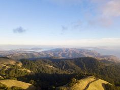 an aerial view of some hills and trees with water in the distance on a sunny day