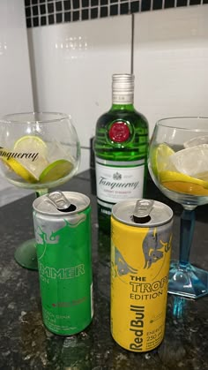 three different types of alcohol sitting on a counter top next to glasses with lemon wedges in them