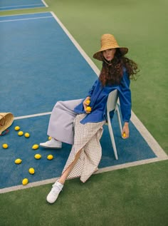 a woman sitting in a chair with tennis balls on the ground and wearing a hat