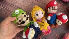 crocheted amigurt toys are being held by someone's hand on a wooden surface