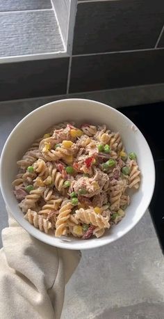 a person holding a bowl of pasta with tuna and peas