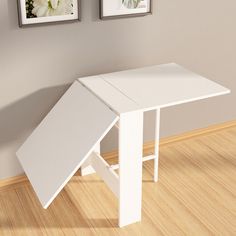 a small white table sitting on top of a hard wood floor next to two framed pictures