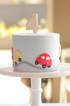 a white cake with cars on it and the number four in the top tier is sitting on a plate