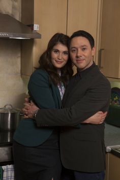 a man and woman standing in a kitchen next to each other with their arms around each other