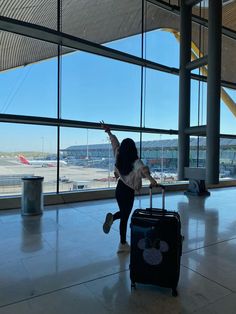 a woman standing in front of an airport window with her hand up to the sky