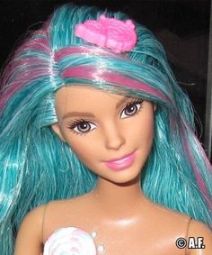 a close up of a barbie doll with blue hair and pink bow holding a lollipop