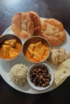 a white plate topped with different types of food on top of a wooden table next to bread