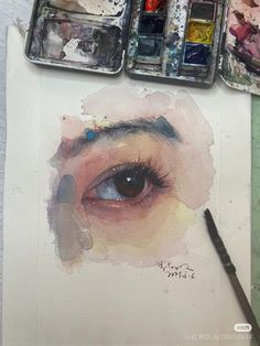 an artist's eye with watercolors and paintbrushes on the table