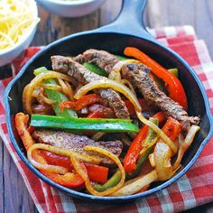 steak fajitas in a skillet with vegetables and guacamole on the side