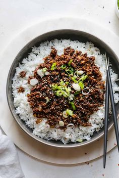 a bowl filled with white rice and ground beef next to chopsticks on the side