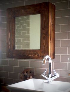 a bathroom sink sitting under a mirror next to a wall mounted faucet in front of a brick wall