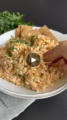 someone is picking up some crackers from a white plate with food on it and garnished with parsley