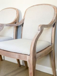 two wooden chairs sitting next to each other on a carpeted floor in front of a white wall