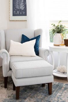 a striped chair with blue and white pillows in front of a painting on the wall