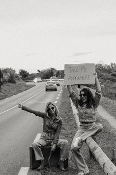 two women sitting on the side of a road holding signs