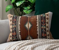 a white couch with a brown and black pillow on it next to a green plant