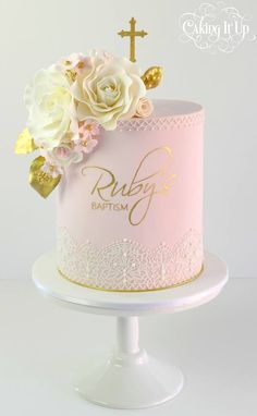 a pink cake with white flowers and gold lettering on the top is sitting on a pedestal