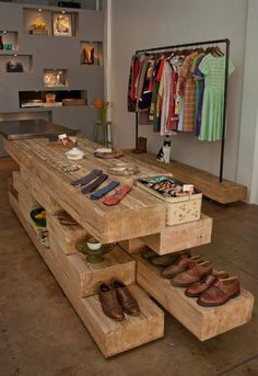 a wooden table with shoes on it in a room filled with shelves and hanging clothes