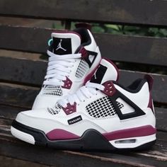 a pair of white and purple sneakers sitting on top of a wooden bench in front of trees